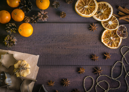 Christmas background frame with tangerines, dried oranges, cinnamon sticks, anise stars, cookie molds. Rustic brown wooden background. Top viewの写真素材