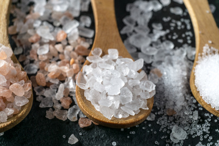 Different types of salt. Sea, himalayan and kitchen salt. Top view on three wooden spoons on black backgroundの写真素材