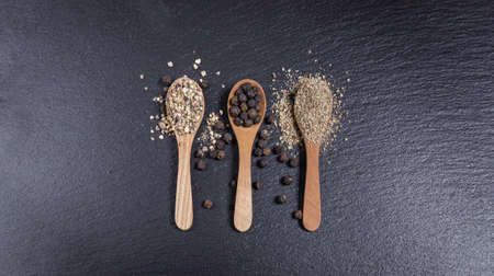 Black whole peppercorns and pepper powder, pepper mix in wooden spoons on dark backgroundの写真素材