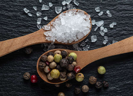 Salt and whole black peppercorns, pepper mix in wooden spoons on dark background, top viewの写真素材