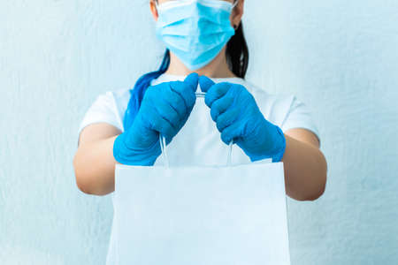 Cropped photo close-up of a girl with blue hair in gloves and a mask holding a package. isolated on a light background. delivery conceptの写真素材