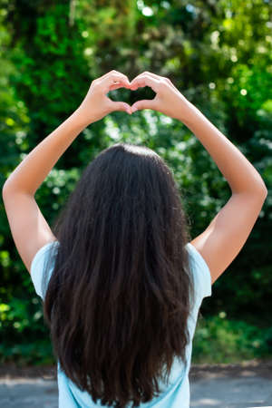 girl with long hair makes a heart symbol with her hands. friendship, love, hope, faith. Indian,...