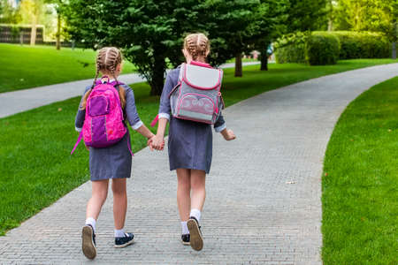 Two elementary school students walk hand in hand. sisters with school bags. Back to school. Little...