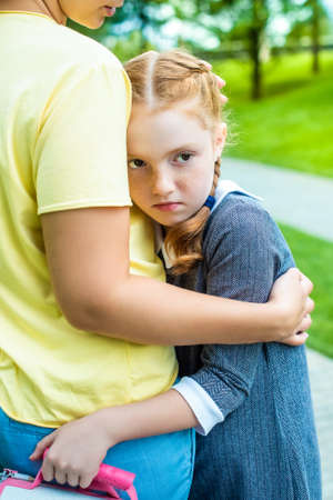 Mom comforting her crying daughter schoolgirl on the way home from school - the concept of...