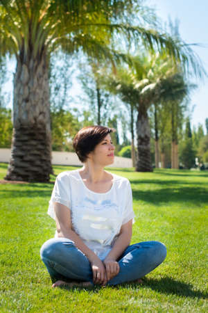 cute adult woman sits on the grass under palm trees. concept of active and happy retirement elderly citizen outdoors.の写真素材