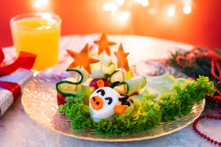 Funny Christmas breakfast, cucumber trees, egg bull. Orange juice. cow symbol of the year 2021. gift, branches, red garland.の写真素材