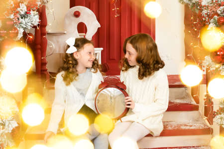 two red-haired sisters on the veranda of a house decorated for Christmas. garland lights, bokehの写真素材