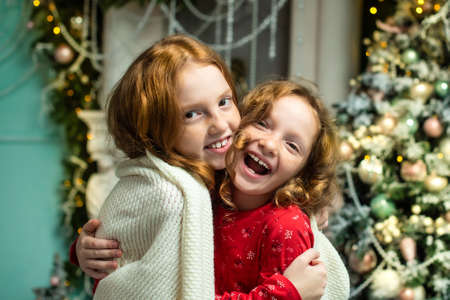 two red-haired sisters on the veranda of a house decorated for Christmas. garland lights, bokeh, smiles, window. festive atmosphereの写真素材