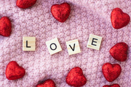 word love on wooden letters and two red shiny hearts. on a pink knitted background. needlework,...