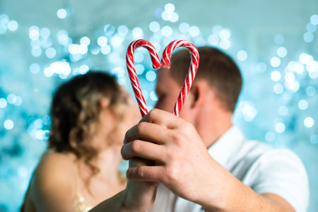 couple in love kissing and heart made of two lollipop. Valentines Day. Hands hold two candy canes making the shape of heart. Heart formed of two white and red Christmas candies.の写真素材