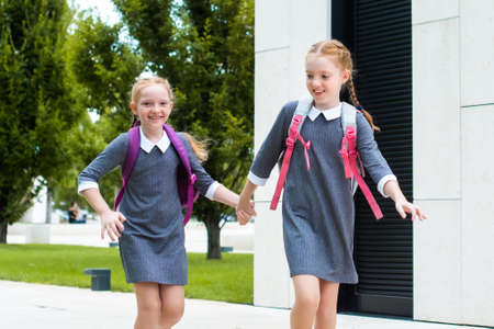 two cute redhead schoolgirls go to school. laugh, chat and run. sisters in school uniformの写真素材
