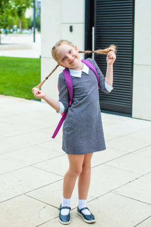 cute redhead schoolgirl laughs, holds herself by her pigtails. happy back to school.