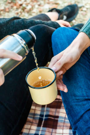 picnic in the autumn forest. female hands pour tea from a into a retro mug. romantic walk fall.の写真素材