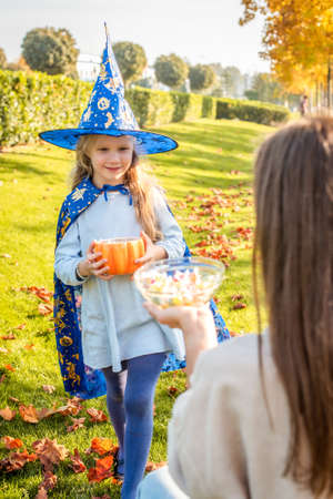 a woman treats a girl dressed as a witch with sweets. child takes sweets for the halloween holiday....