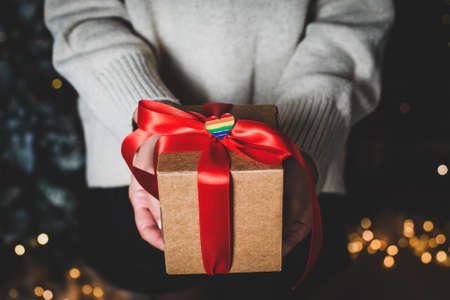 Woman holds gift with red ribbon and heart-shaped icon in hand. craft box and garland