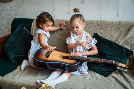 white and black girls on a couch and plays the guitar. babes is playing, composes melody and music.の写真素材