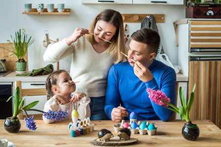 the family paints colorful Easter eggs. mom, dad and daughter celebrate spring holiday togetherの写真素材