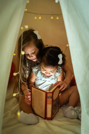 two girls are reading a book in a tent with a garland. baby with black and white skin color studyの写真素材