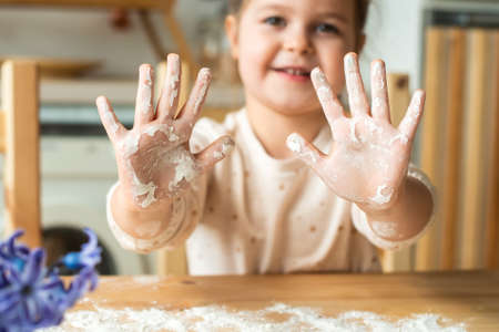 girl cooks at home. in a bright kitchen, a child stirs flour on the table. baby helps mom and laughsの写真素材
