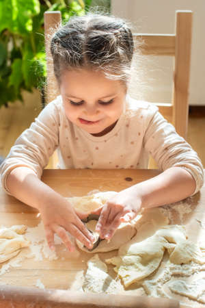 girl cooks at home. in a bright kitchen, a child stirs flour on the table. baby helps mom and laughsの写真素材