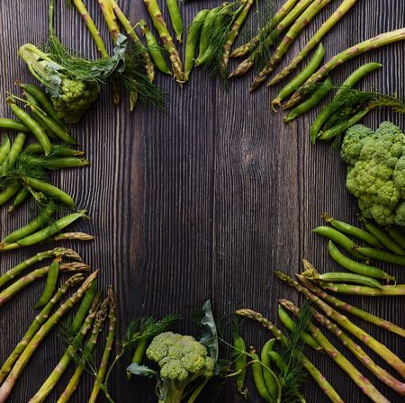Frame with Fresh Green food, Green vegetables on wooden board. Composition on a dark wooden background of green organic vegetarian products: peas, dill, broccoli, asparagus. Top view.の写真素材