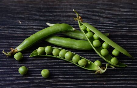 Fresh green pea pod with beans isolated on dark wooden background. Fresh pods of green peas horizontal composition isolated on a old rustic wooden surface, soft focusの写真素材