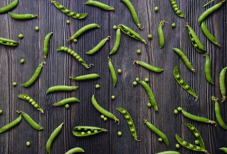 Peas in pods pattern. Top view of fresh vegetable on a dark wooden background green pea pod with beans isolated. Horizontal composition isolated on a old rustic wooden surfaceの写真素材