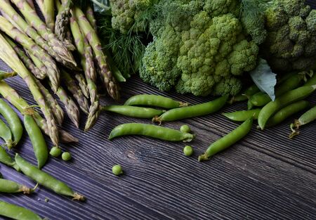 Composition on a dark wooden background of green organic vegetarian products: peas, dill, broccoli,...