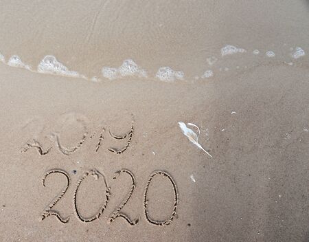 New Years 2020 replace 2019 concept. End of 2019 Happy New Year 2020, lettering on beach with wave...