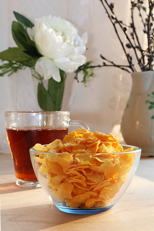 A mug of tea, a cup of corn and a cake on a sunny table, a bouquet of spring flowers for mood, diet...