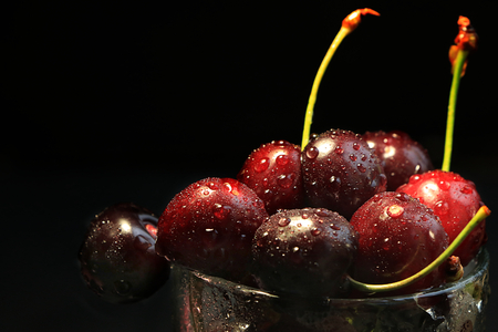 Juicy red cherry with drops on a black background close-up, selective focus. Delicious beautiful berries in a glass after washing make you want to eat themの写真素材