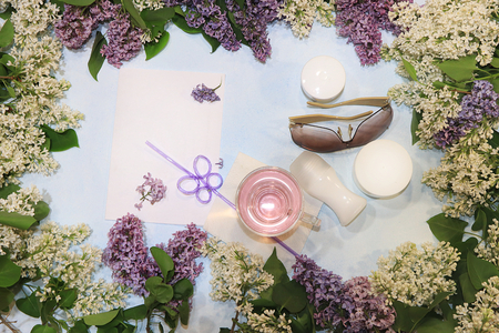 Colorful lilac branches on a blue background with juice, skin care creams, deodorant and glasses, flat lay. Preparing for summer vacation, top view with copy space.の写真素材