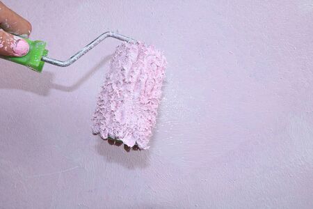 A hand with a roller on the background of a painted wall. Painting the walls during the repair and manufacture of photophones with their own hands. Repair work in the new house, brushes, paints and putty for the necessary workの写真素材