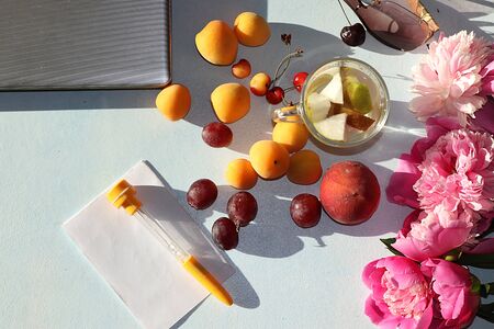 Apricot and orange juice, apricots, grapes on a sunny table next to a laptop, copy space, top view, flat lay. Summer drinks and fruits during a break at work with colorful peony branches, selective focusの写真素材
