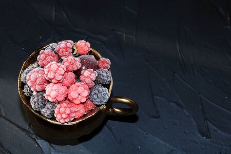 Juicy red raspberries with hoarfrost on a black background, selective focus, top view. Delicious beautiful berries in a glass after washingの写真素材