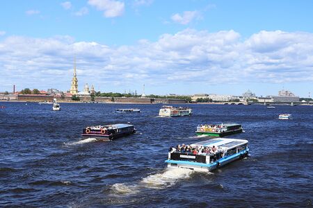 Russia, Petersburg, June 29, 2019. Spit of Vasilyevsky Island. The photo shows the Peter and Paul Fortress on the bank of the Neva against the sky and a pleasure boat with tourists admiring the view of the city.のeditorial素材