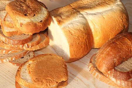 Loaf and slices of fresh white and black bread on a sunny rustic table, diet food, selective focus....