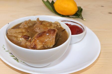 Closeup of meat goulash in a light cup on a wooden table with lemon, rustic simple style, selective...