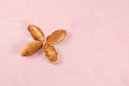 Four fresh rosy croissants on a pink table with breadcrumbs., Top view, place for text. Minimal...