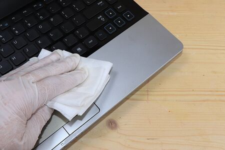 At home in the workplace, a gloved hand wipes the computer with a disinfectant solution. Covid 19. Hygiene, protection against epidemics, coldsprotection conceptの写真素材