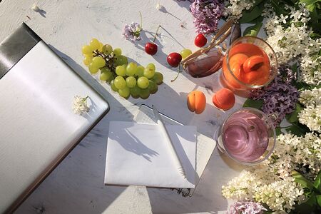 Computer and bird cherry on a sunny table, remote work, minimal business concept. Home office, cozy women's desk, apricot juice and glasses,の写真素材