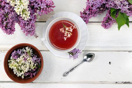 Cup of flower tea with a branch of lilac flowers and pink water in a wooden cup on a white wooden background, flat lay, concept of healthy eating. Place for text,の写真素材