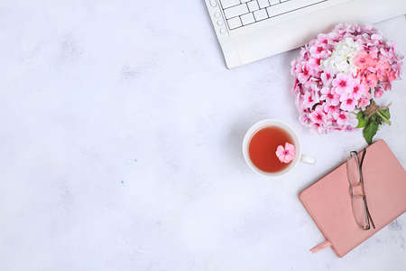 Work desk of a modern woman, home office. Notepad, tea, spring flowers on a light table. Minimal...