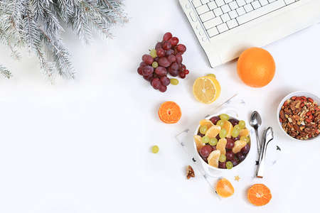 Modern woman work desk, healthy breakfast, home office. Computer, Christmas decorations, fruit salad and a cup of tea on a light table. Lifestyle concept, flat layの写真素材