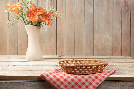 Empty wooden table with basket and vase of flowers for product presentation, rustic style, summer or autumn layout for design, summer flower arrangement, place for text, selective focusの写真素材