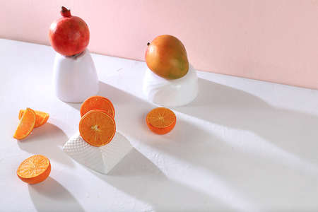 Modern still life with citrus, orange juice and oranges, pomegranate and mango on stand and podiums on pink background with long hard shadows, minimal detox diet concept, summer vitamin drinks, selective focusの写真素材