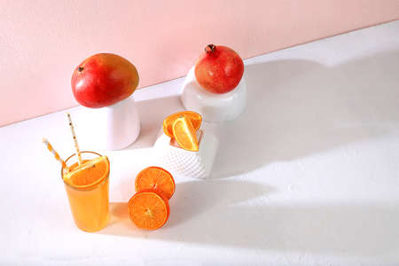 Modern still life with citrus fruits, orange juice and ingredients on a colored pink background with long hard shadows, minimal detox diet concept, summer vitamin drinks, selective focus, place for textの写真素材