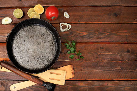 Kitchen wooden table with a frying pan for frying cutlets, meat, burgers. Cooking background with tomato, onion, garlic and herbs, place for text, food design, rustic style, advertisement of a cafe, restaurant, menu, selective focusの写真素材