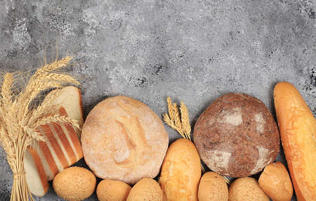Assortment of homemade sourdough bread with crispy crust and ears of rye and wheat on gray concrete background with place for text, modern bakery concept, top view, healthy natural food, selective focusの写真素材