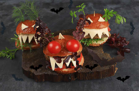 Halloween food concept. Scary burgers with fresh parsley leaves, tomatoes, cream cheese, onion and cutlet on old concrete background, low key, food delivery, cafe advertisement, menu, selective focus,の写真素材